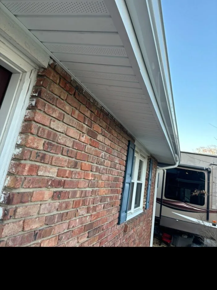 Clean white vented soffit and gutters on brick house side view after replacement