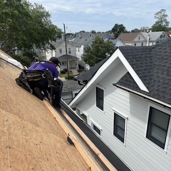 Crew member in a safety harness on a roof deck with a finished gray shingle roof in the background