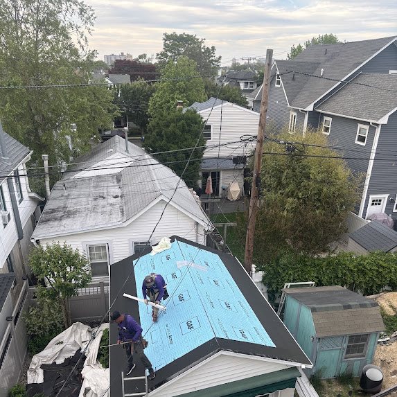 Aerial view of crew installing blue GAF Deck-Armor underlayment on a shed roof in a Bradley Beach backyard