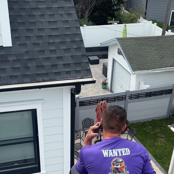 Crew member beside a finished dark shingle roof and new gutter with a paver patio below