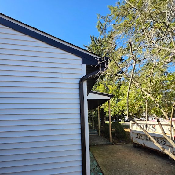 Black downspout coming off the gable end of a new home in Brick beside a construction dumpster