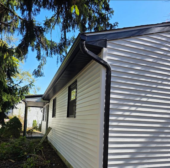Black gutter and elbowed downspout at the rear of a Brick NJ home under tall pine trees