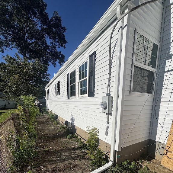 Long side of a white new construction home with a downspout running past the electric meter
