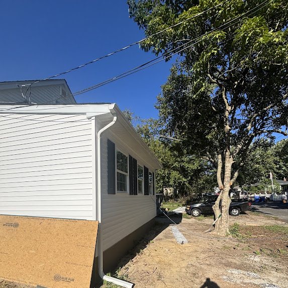 White downspout at the rear corner of a new construction home with exposed sheathing at the base