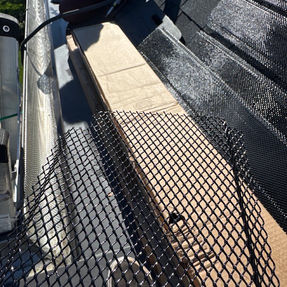 Stainless steel gutter guard mesh being cut to fit on a roof during installation