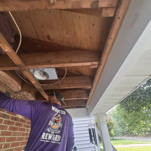 Crew member working on exposed porch framing during a soffit replacement