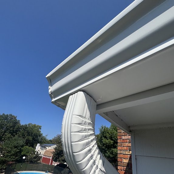 White gutter corner installed above a scalloped aluminum awning beside a brick chimney