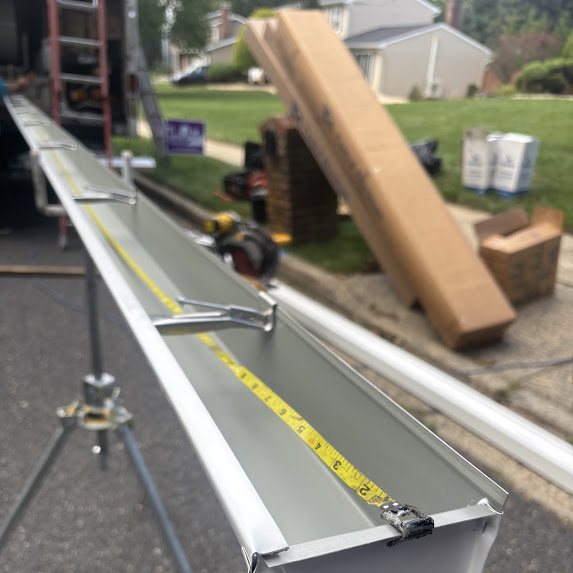 Seamless white 6-inch K-style gutter being fabricated on stands in the street with a tape measure