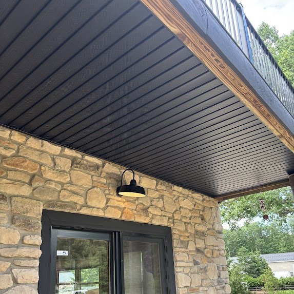 Black soffit with barn-style light fixture against stone wall