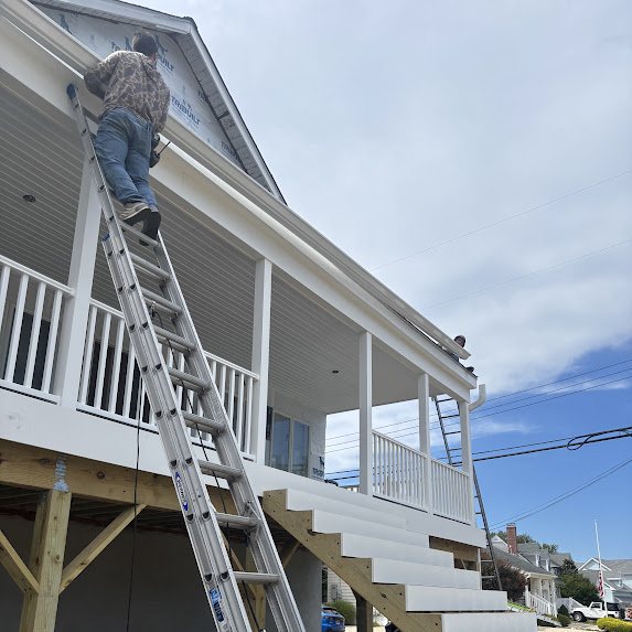 Crew member on a ladder installing gutters at the gable of a new construction shore home