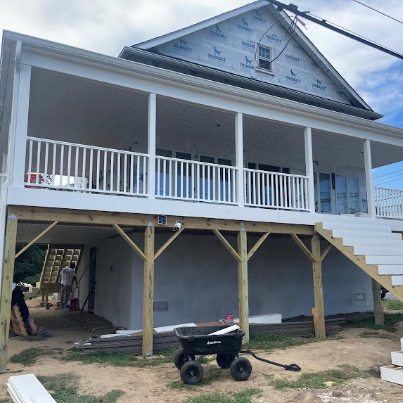 Covered porch of a new shore home with white railings and new white 6-inch gutters
