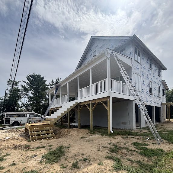 Full side view of an elevated new construction home in Manasquan with wraparound porch and white gutters