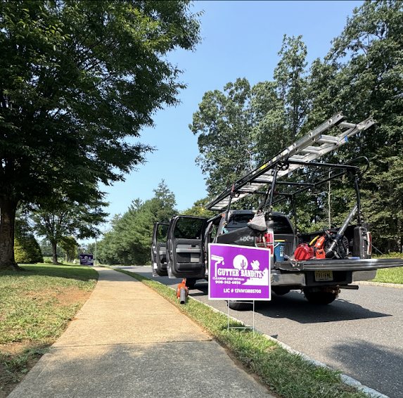 Gutter Bandits truck with ladders and purple yard sign on a Marlboro street