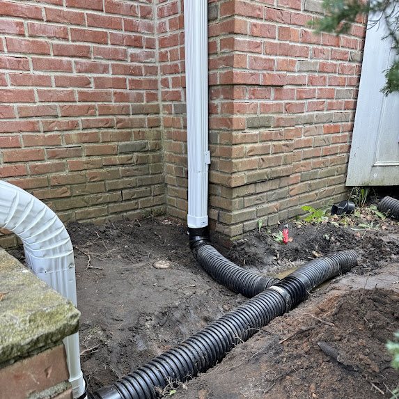 White downspout connected to underground corrugated drainage pipe at a brick wall