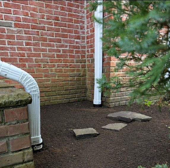 New white downspouts feeding an underground drainage system beside a brick home in Marlboro NJ