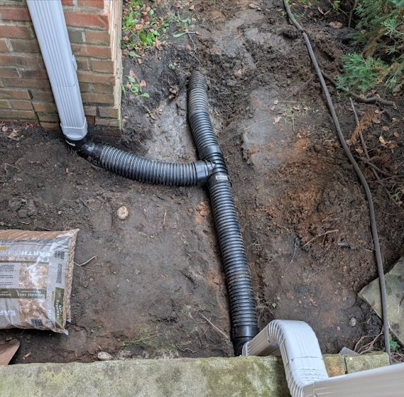 Corrugated drainage pipe tee junction in a trench beside a Marlboro home