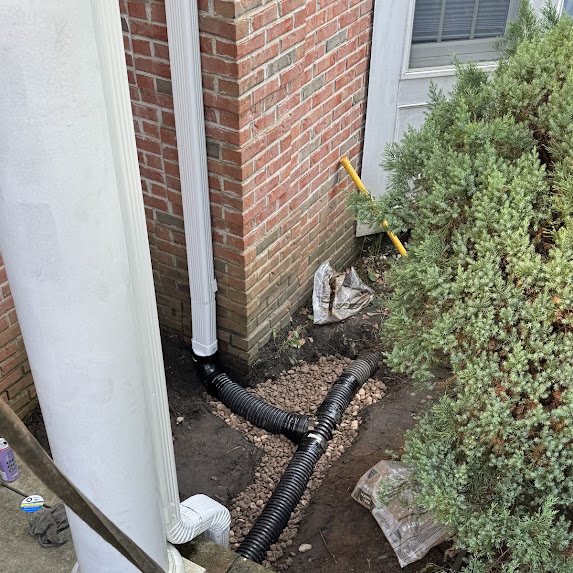 Drainage rock around corrugated pipe junction at a downspout in Marlboro