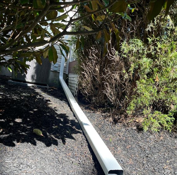 White downspout extension running through a mulched planting bed away from the foundation