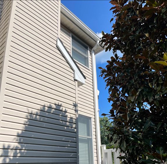 White 3x4 downspout on the side of a house beside a magnolia tree