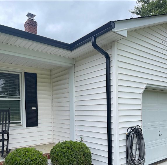 Black 2x3 downspout at the corner between a porch and garage on a white house