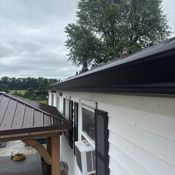 New black gutter run along a white house beside a dark standing-seam metal patio roof