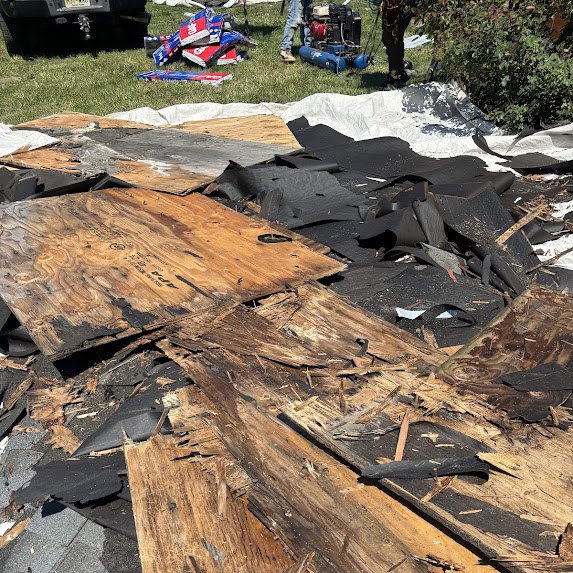 Tear-off debris and rotted plywood on protective tarps at a ranch roofing job