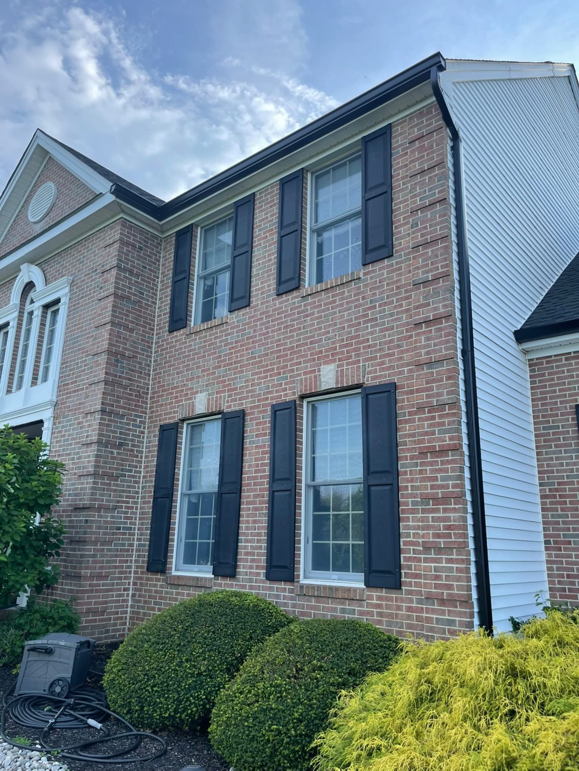 Black downspout on the corner where brick meets white siding