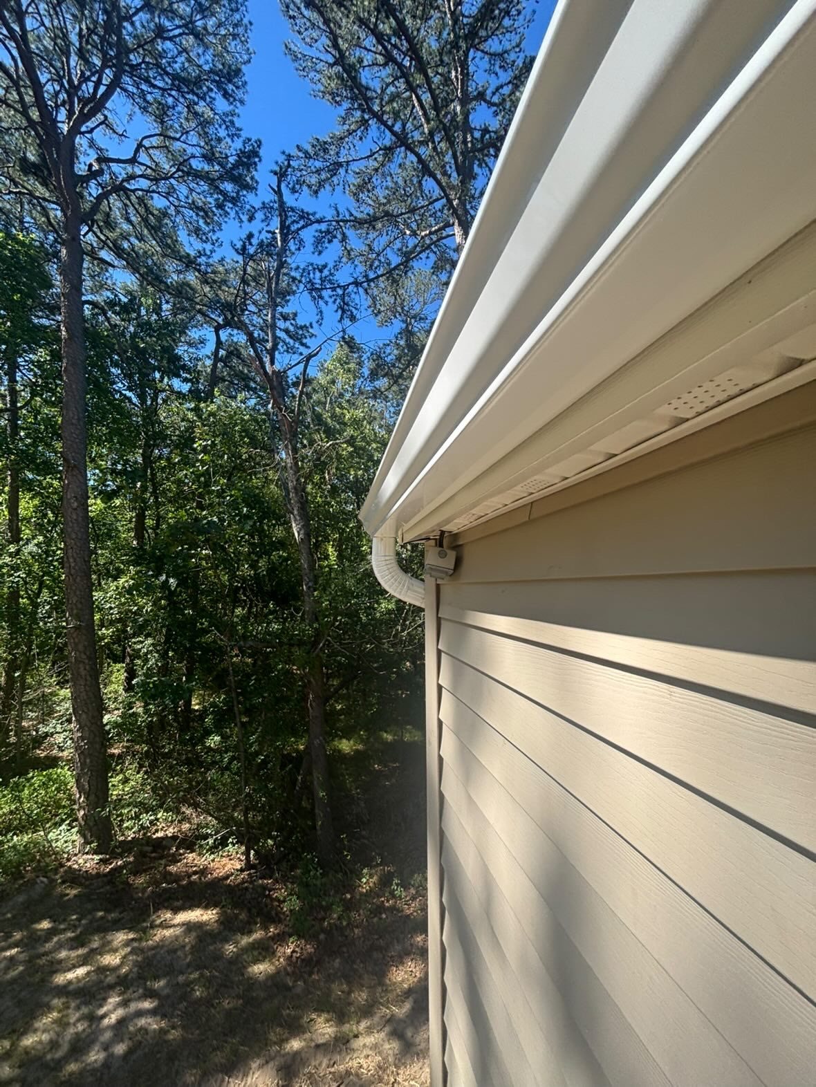 New white gutter and downspout on a renovated tan ranch in Millstone Township, surrounded by trees