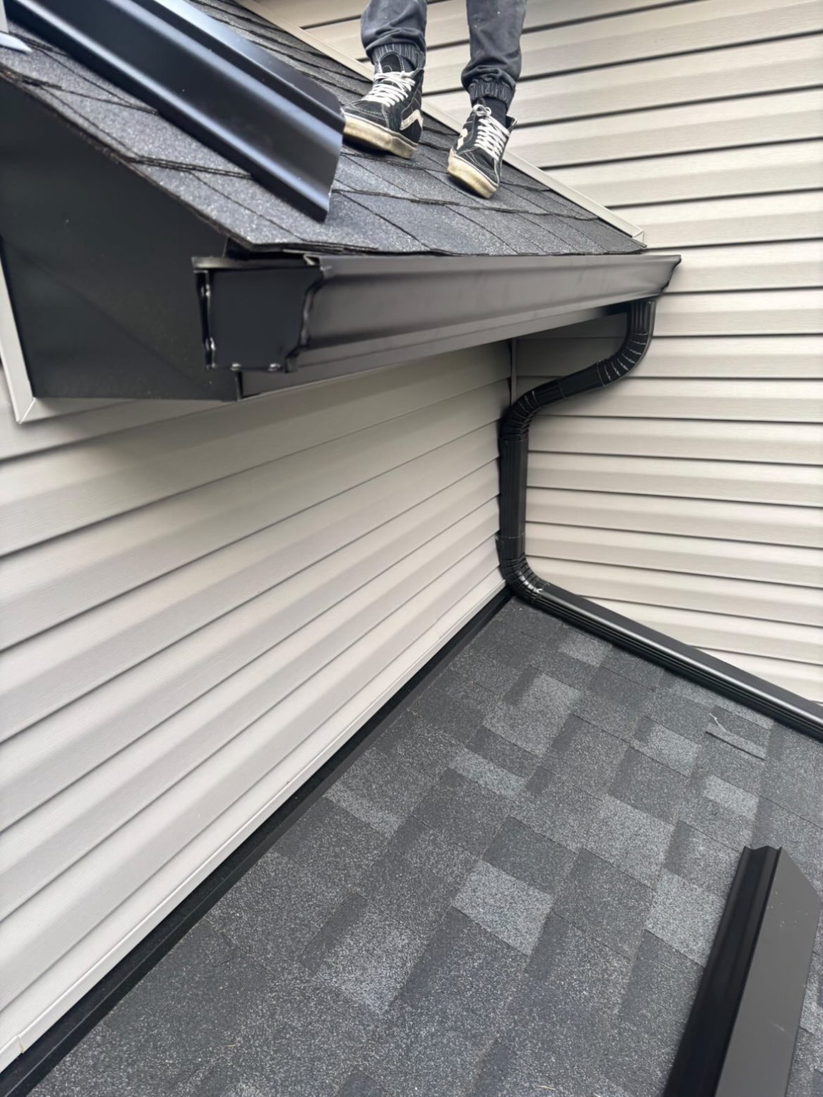 Black gutter corner and downspout detail on a vinyl-sided home
