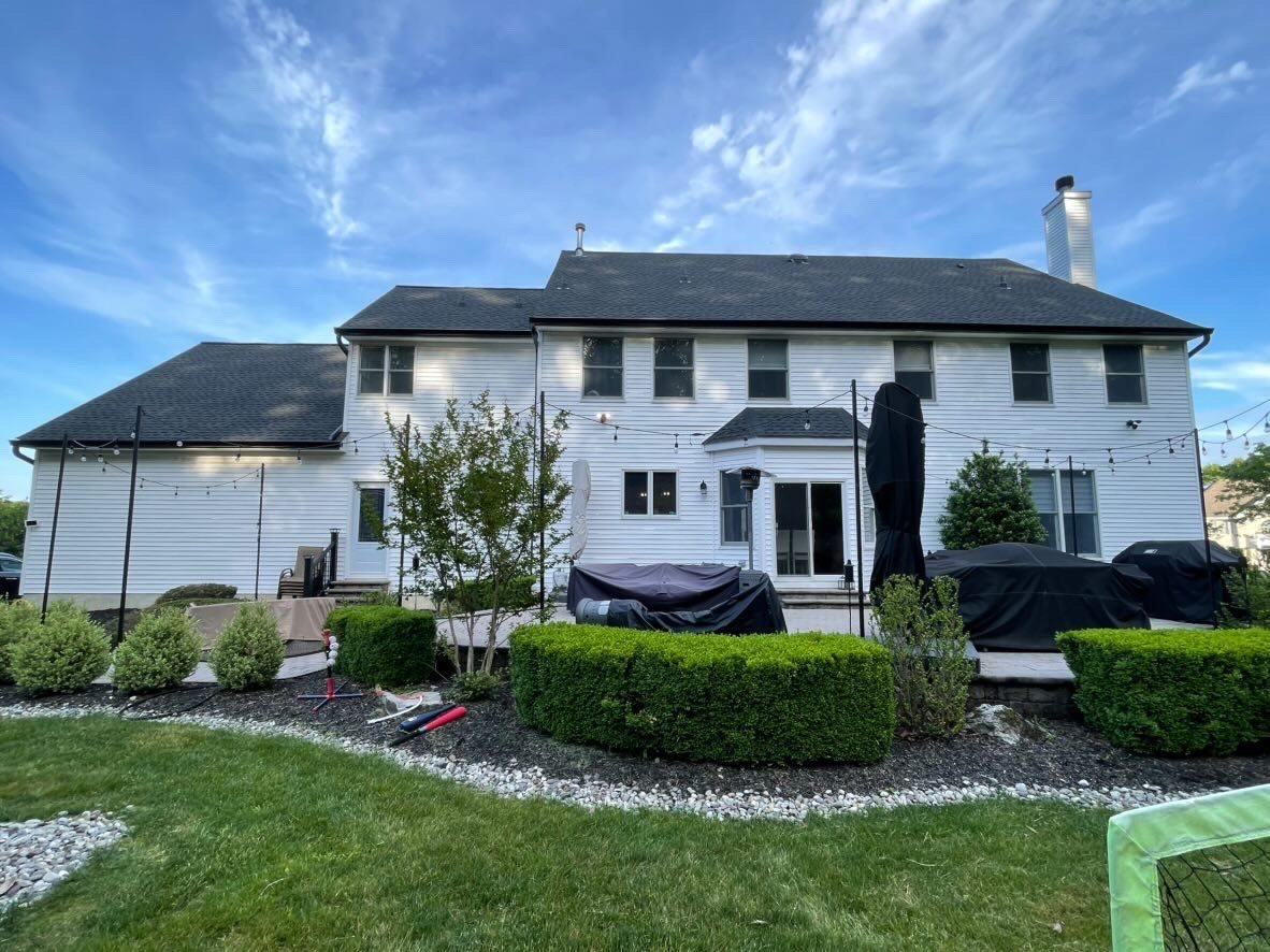 Large white colonial in Millstone Township from the rear, with new black gutters above a patio