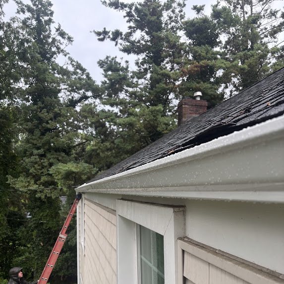 Crew installing a new white gutter on a roof edge in the rain