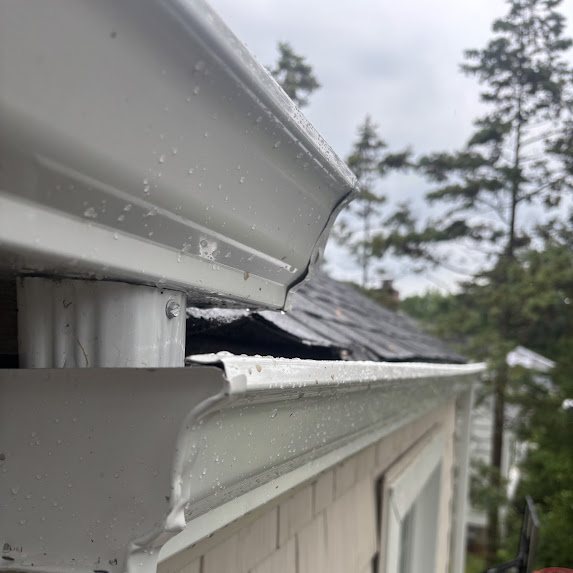 Close-up of a new white gutter and downspout with rain drops