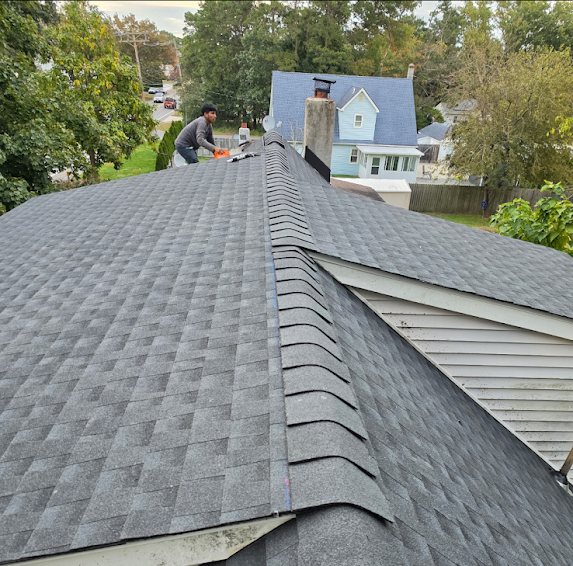 Crew member installing ridge cap shingles on a finished GAF Charcoal roof in Toms River